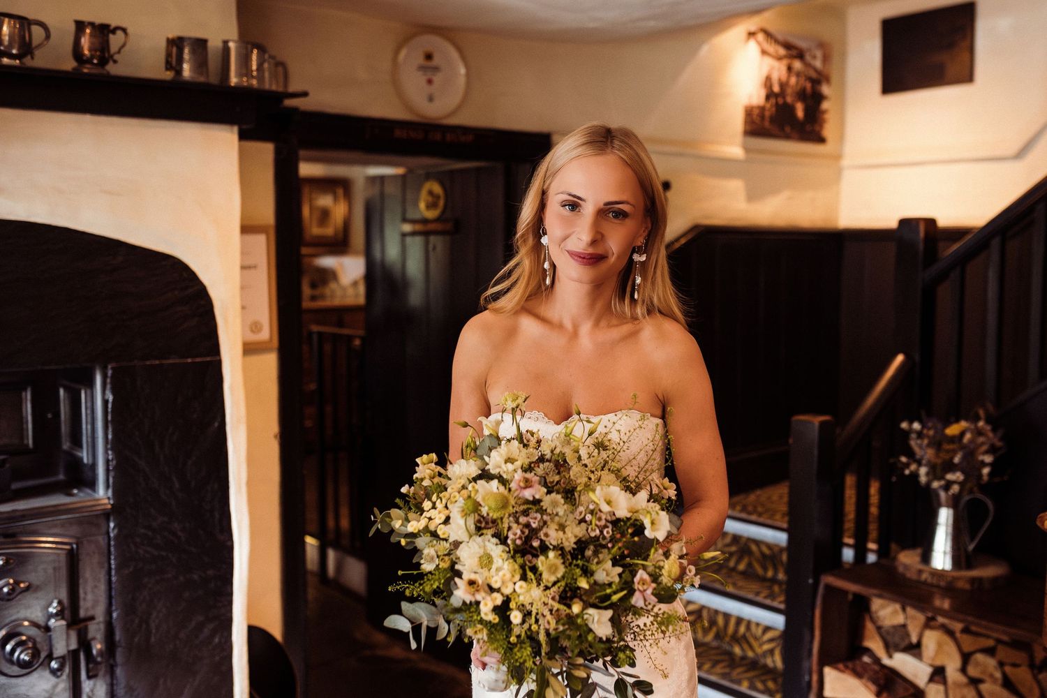 A bride in a strapless wedding dress holds a beautiful white and yellow bouquet inside a rustic cottage interior.