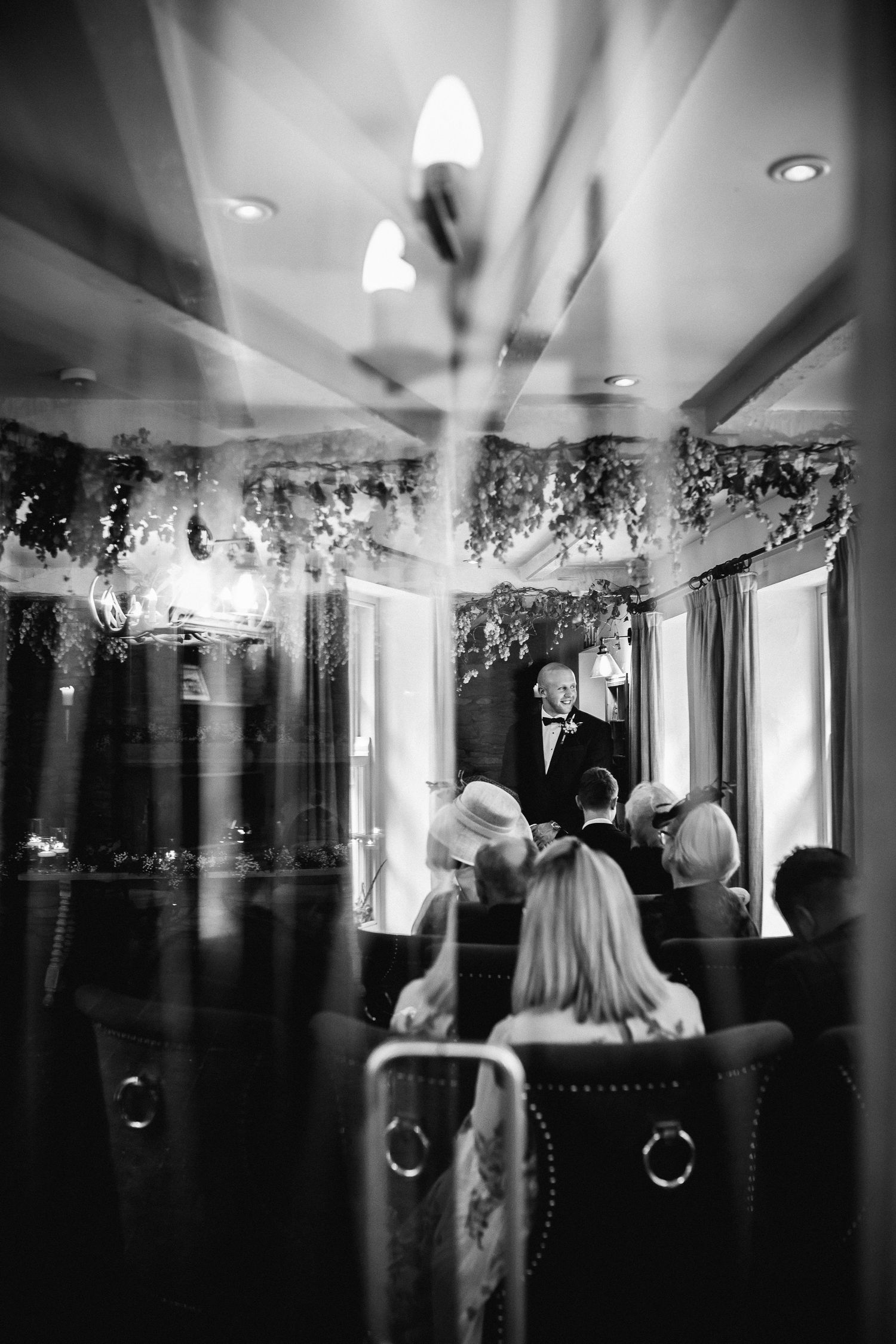 Black and white panoramic view of a wedding reception venue with twinkling lights and silhouettes of guests.