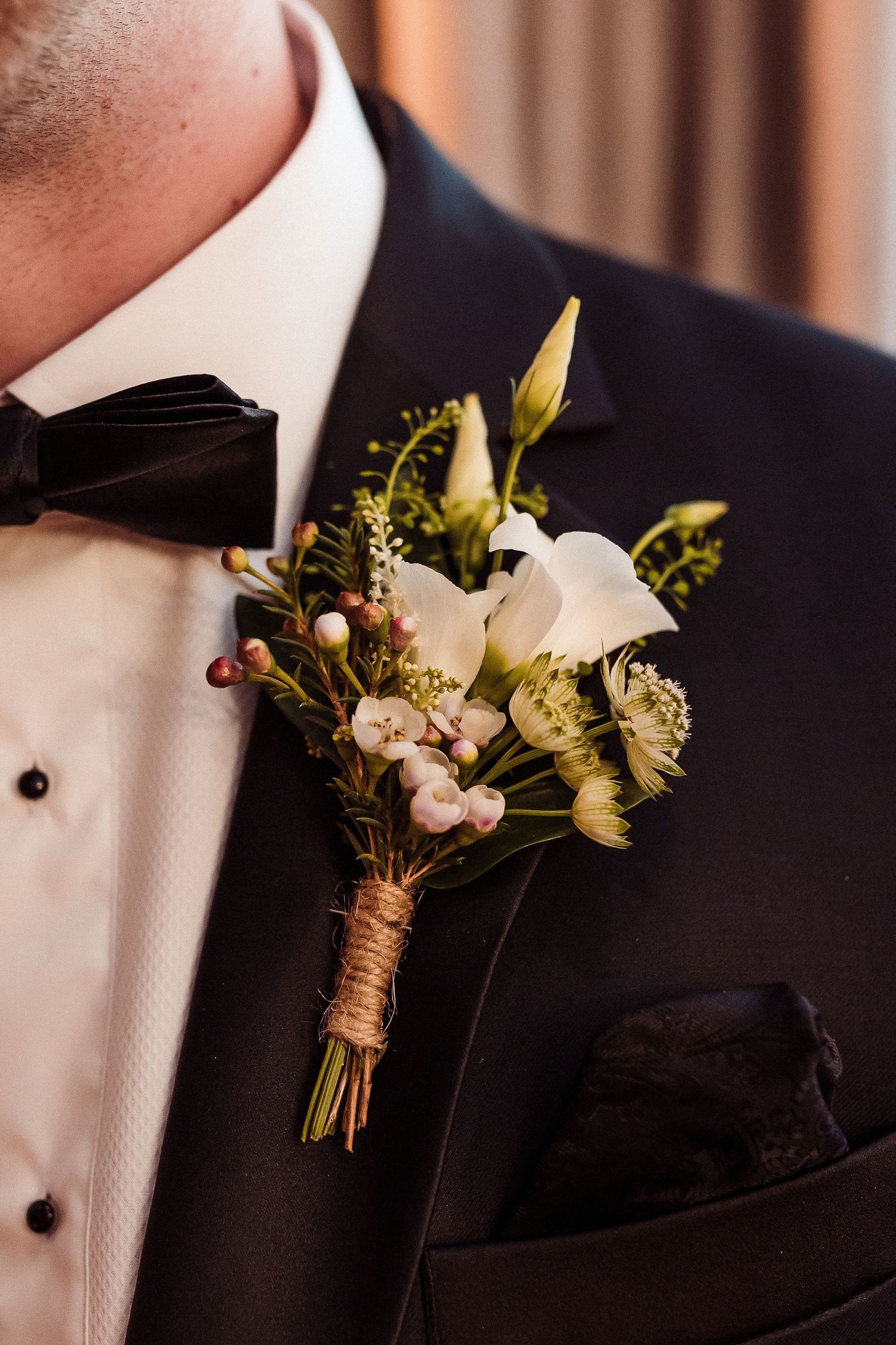 Close-up of white calla lily and yellow floral boutonnieres with twine wrap on black tuxedo lapels.
