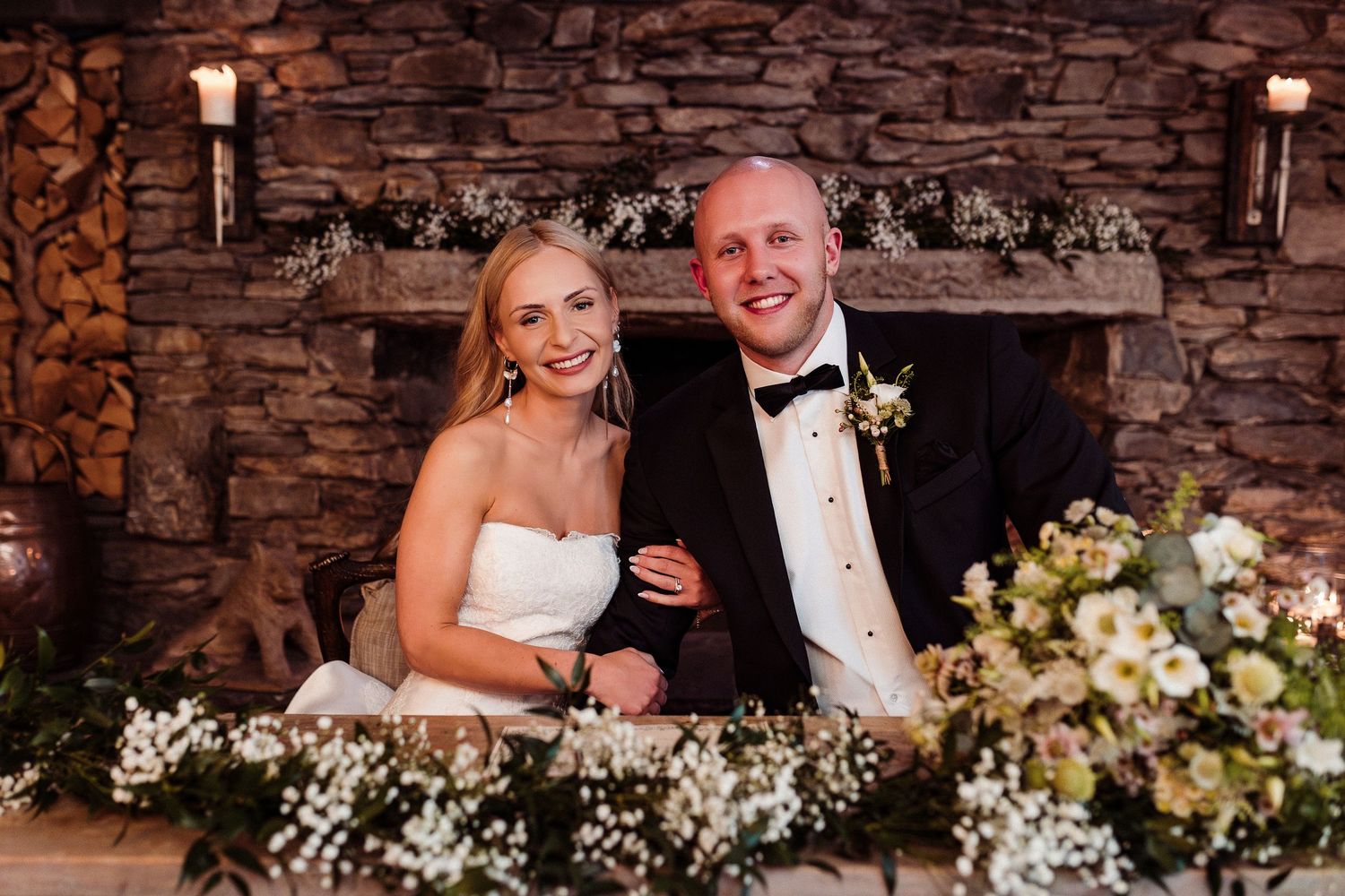 Wedding party posing against rustic stone wall backdrop with floral decorations.
