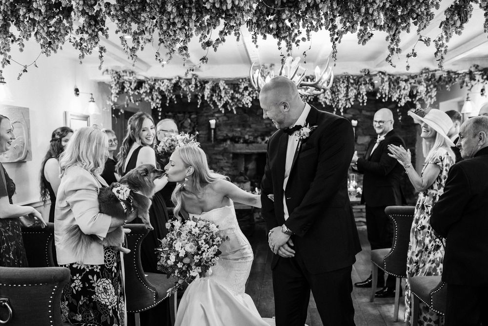 Wedding guests dancing and celebrating under hanging floral decorations at an indoor reception venue.