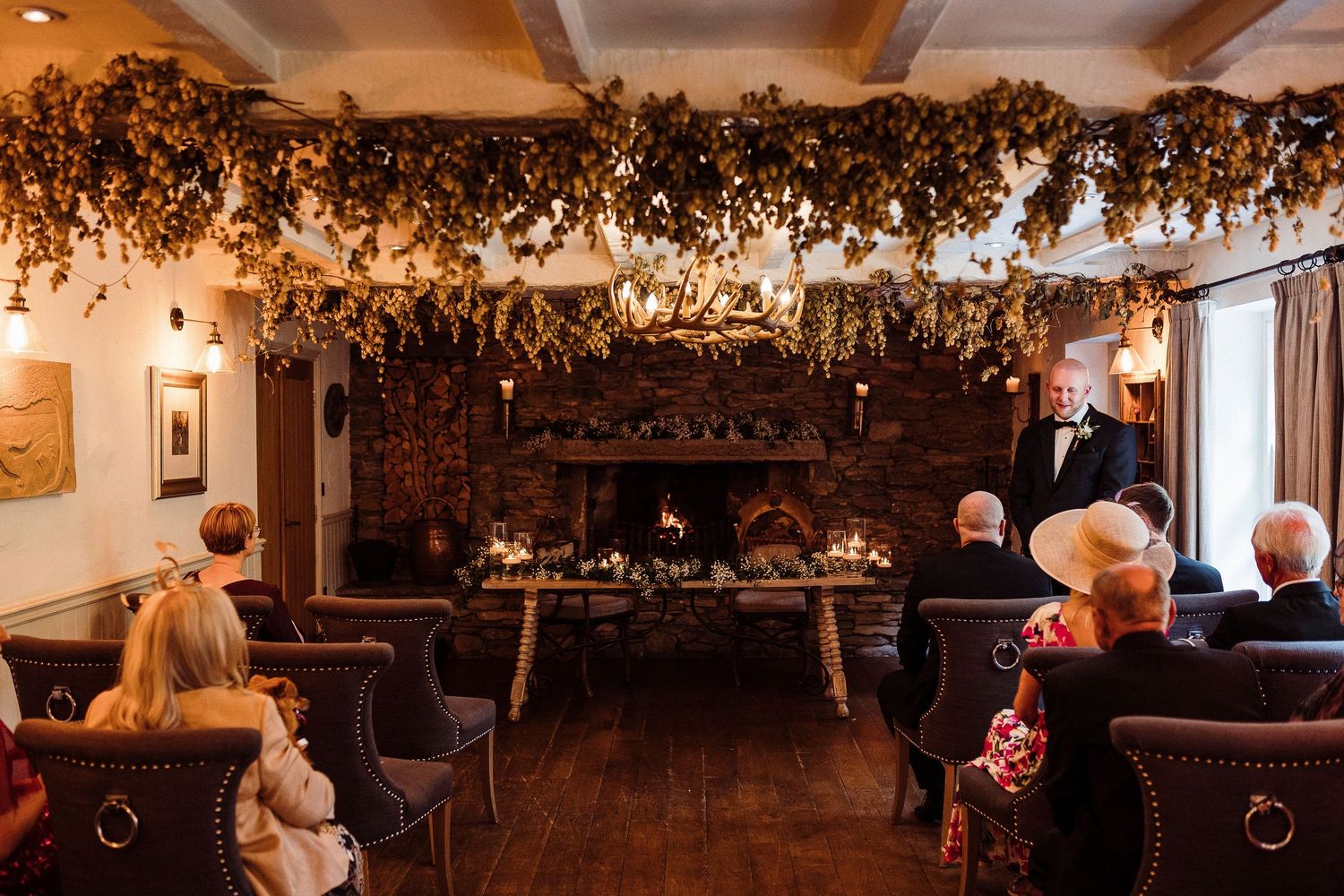A rustic wedding reception venue with warm lighting and dried floral arrangements hanging from wooden beams.