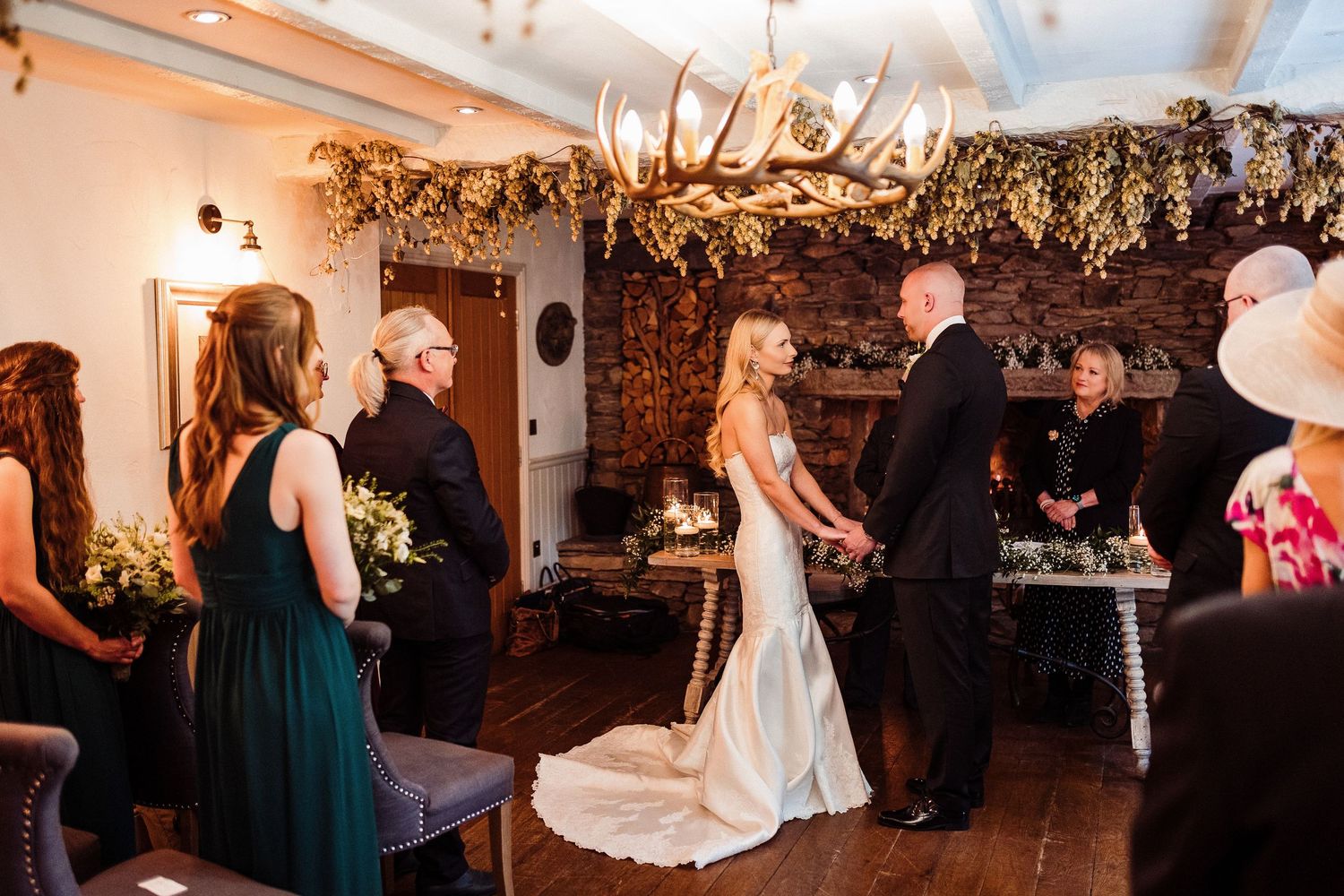 Wedding ceremony taking place in a rustic indoor venue decorated with dried floral arrangements hanging from above.