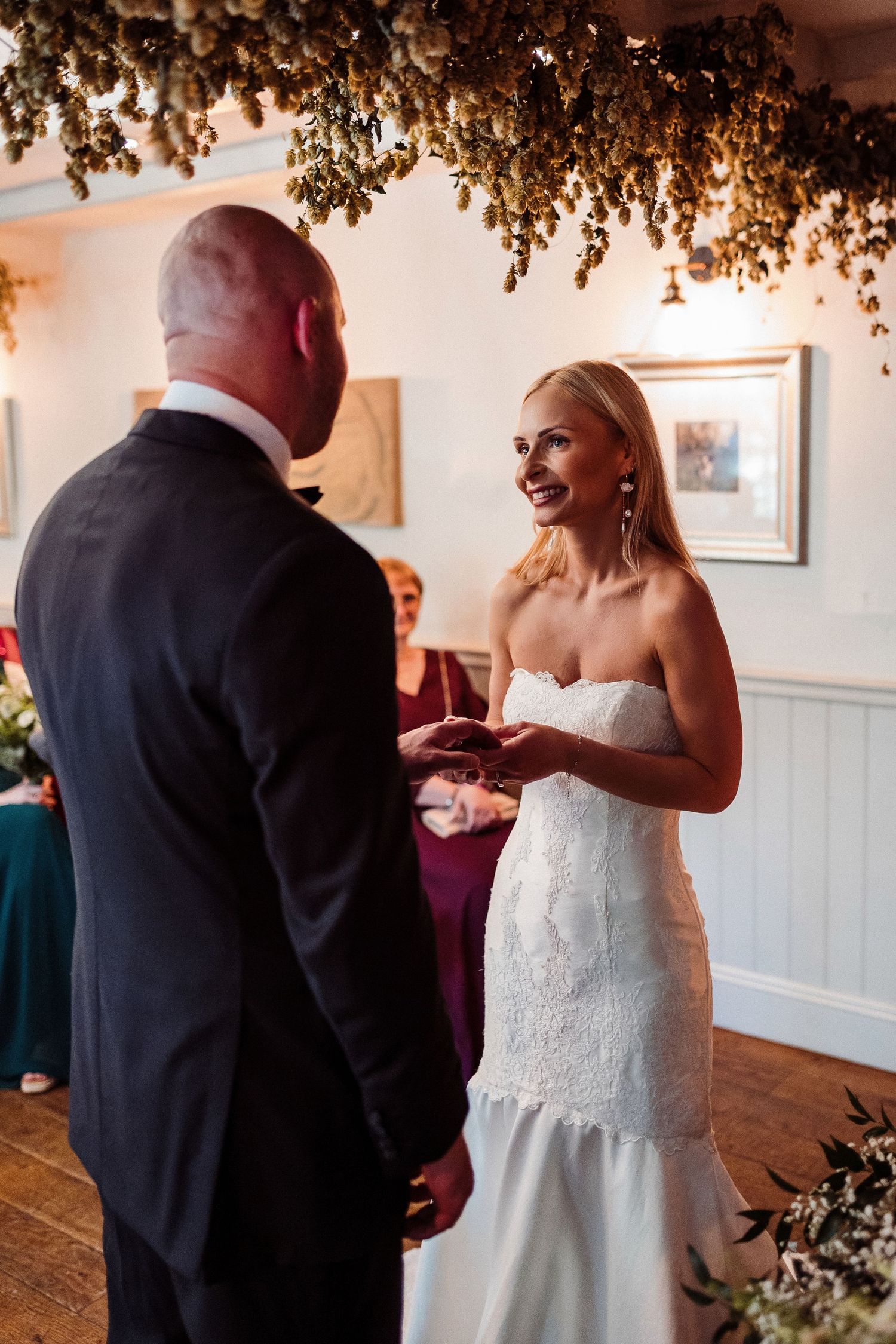 Couple exchanging vows during an intimate indoor wedding ceremony beneath dried floral ceiling decorations.