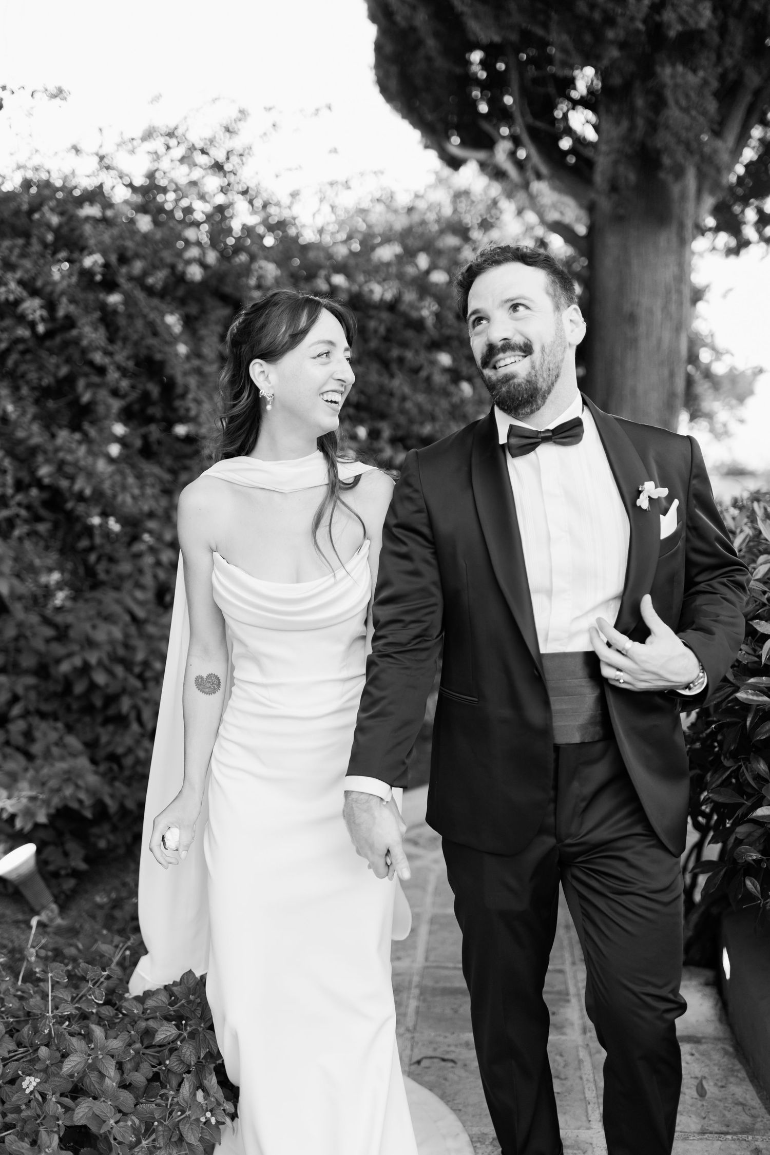 Black and white wedding photos showing a couple in formal attire sharing joyful candid moments outdoors.