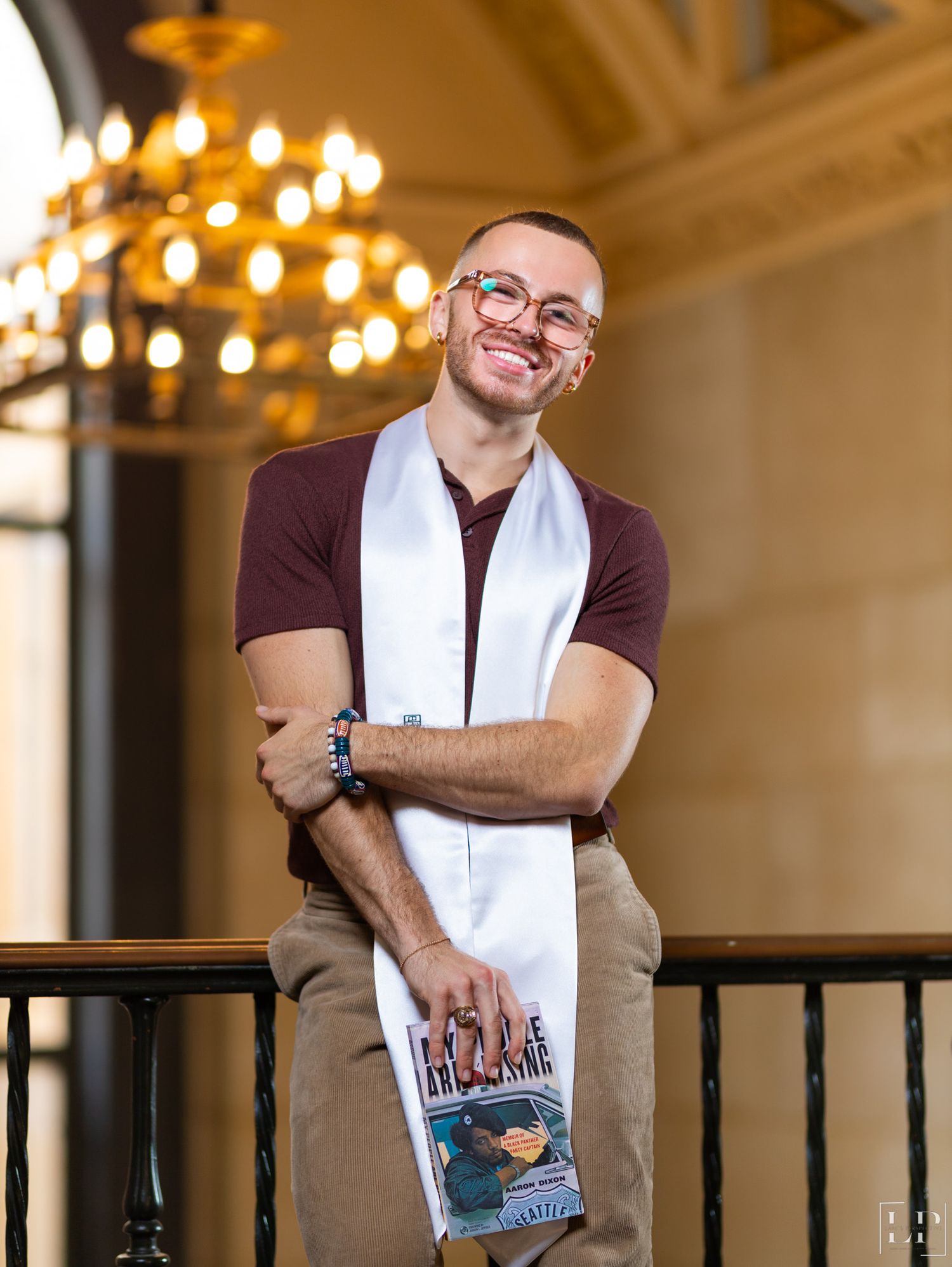 Person with glasses and towel around neck poses against warm-lit interior background.