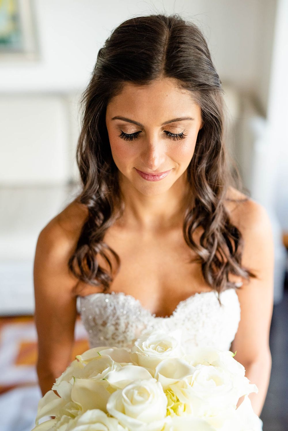 Bride holding white rose bouquet in lace wedding dress with romantic wavy hairstyle.