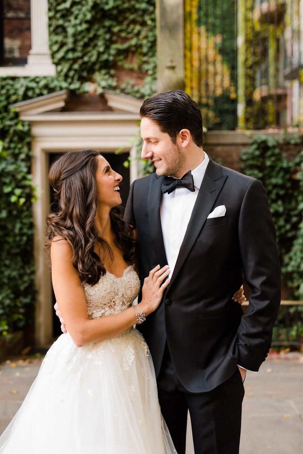 Romantic wedding portrait of couple in formal attire against ivy-covered wall.