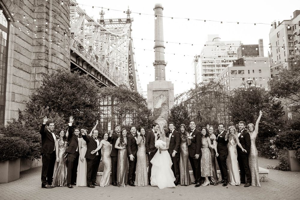 Wedding party in formal attire lined up on city street with urban architecture.