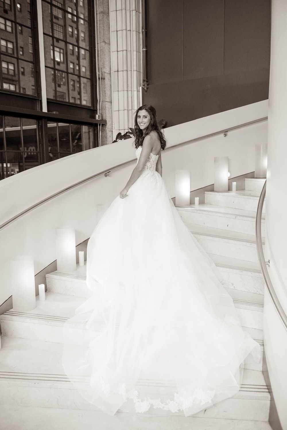 Bride in flowing ballgown poses on illuminated curved staircase.