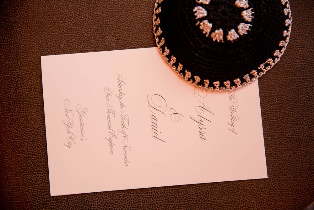 Wedding invitation and black kippah on brown leather surface.
