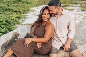 A couple in coordinating earth-tone outfits shares tender moments together on a gravel path outdoors.