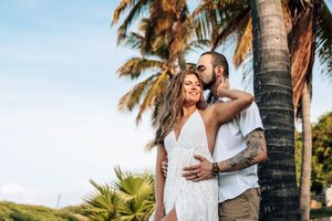 A couple embraces under palm trees at sunset on a tropical beach during a romantic photo session.