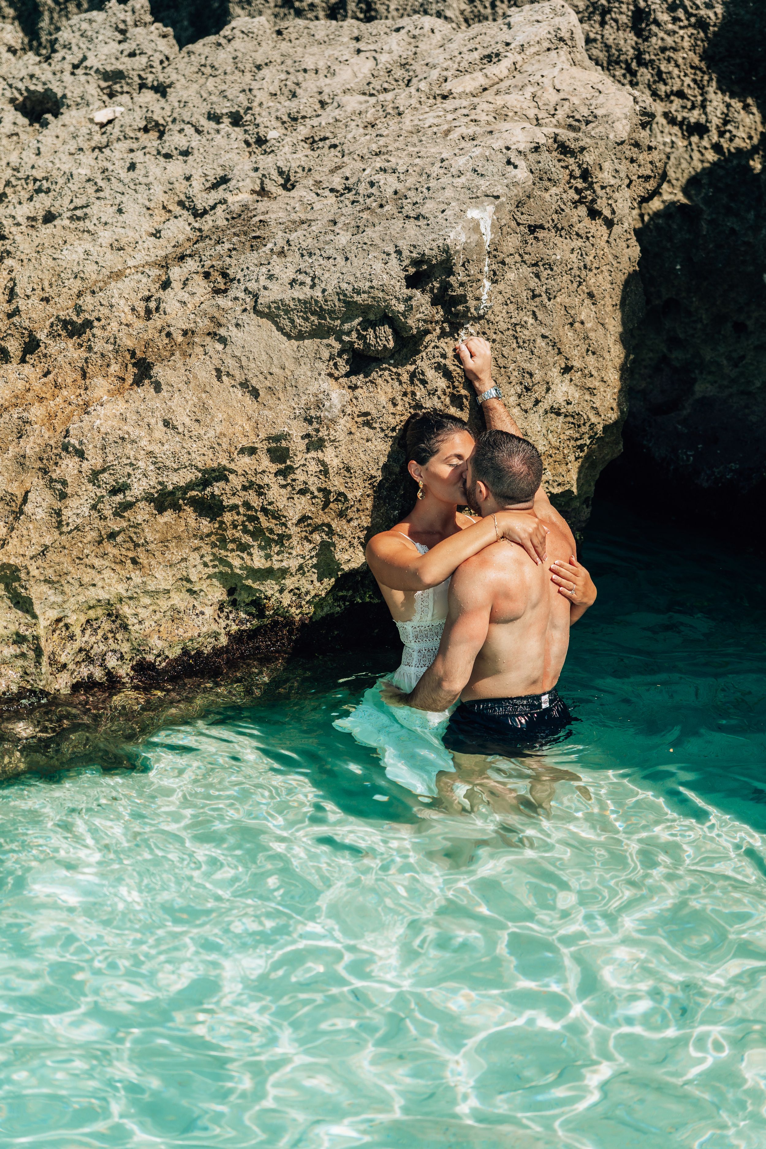 A couple shares an intimate moment while swimming in crystal clear turquoise waters surrounded by rocky cliffs.