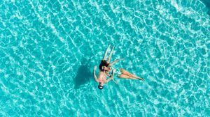 Aerial view of swimmers floating in crystal clear turquoise water of a tropical swimming pool.