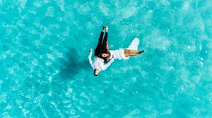 Aerial view of surfers riding waves in crystal clear turquoise ocean waters.