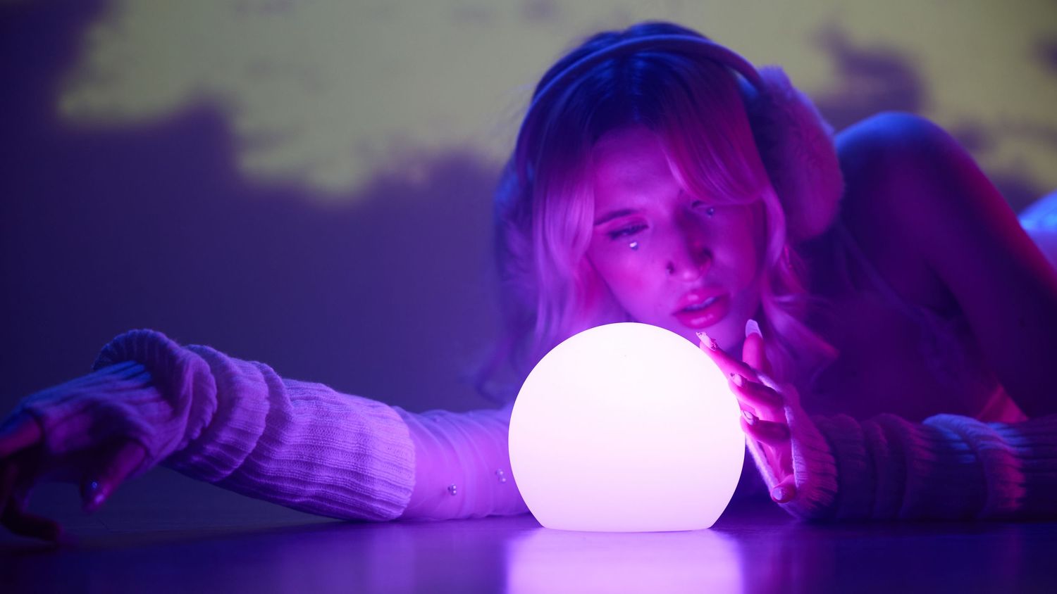 Woman with blonde hair gazing at a glowing white orb in purple neon light ambiance.