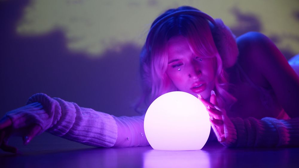 Woman with blonde hair gazing at a glowing white orb in purple neon light ambiance.