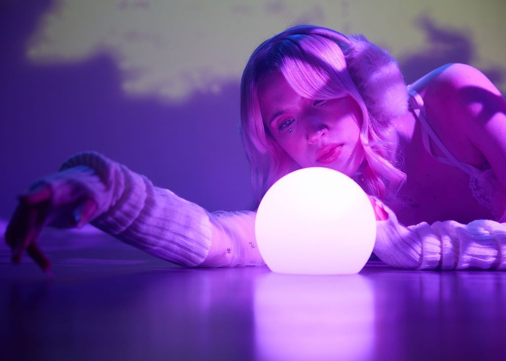 Woman lying down gazing at a glowing white orb in purple neon light ambiance.