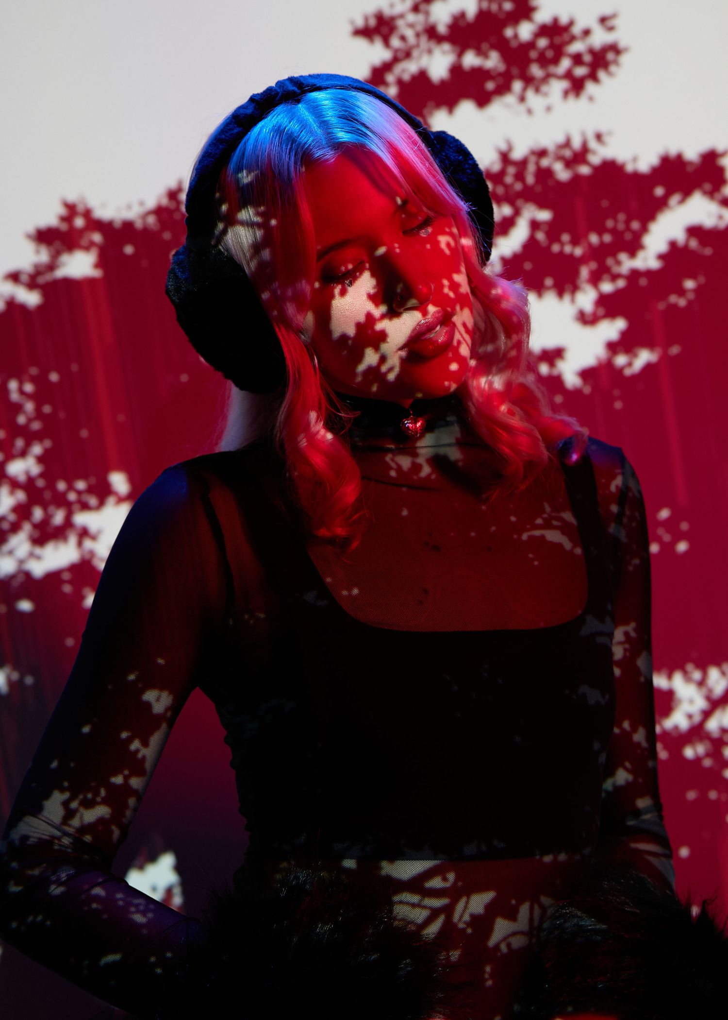 Woman wearing headphones bathed in dramatic red light with floral projections creating an artistic, moody atmosphere.