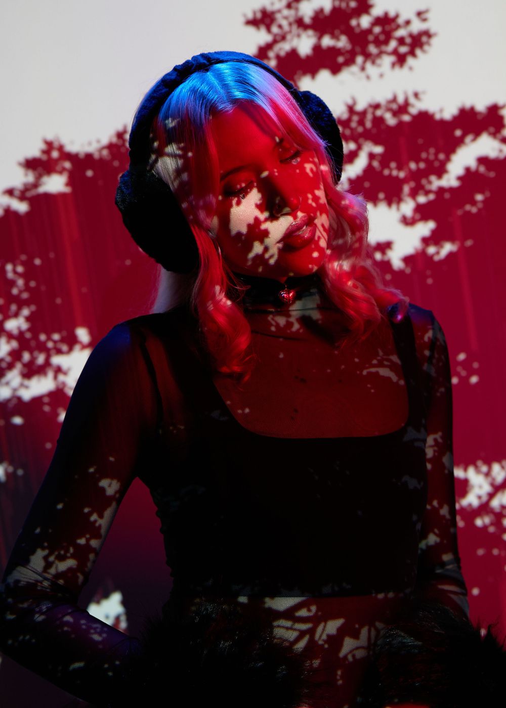 Woman wearing headphones bathed in dramatic red light with floral projections creating an artistic, moody atmosphere.