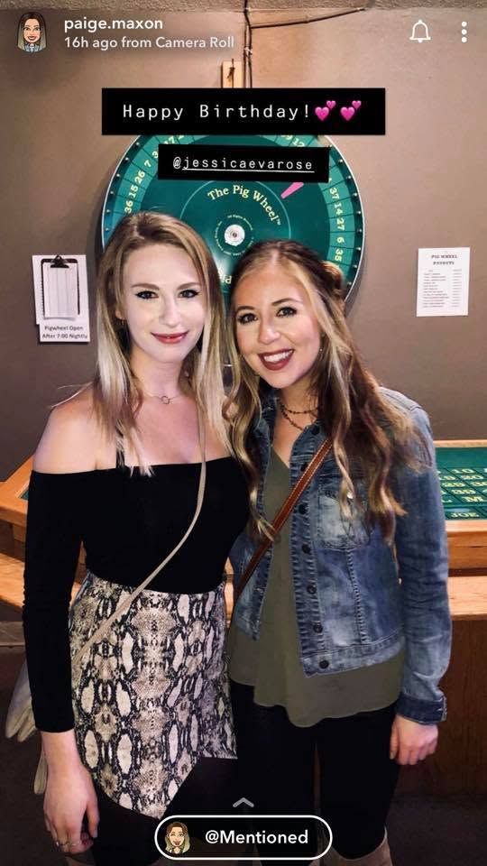 Two women posing together at a birthday celebration in front of a pie wheel game at a bar or restaurant.