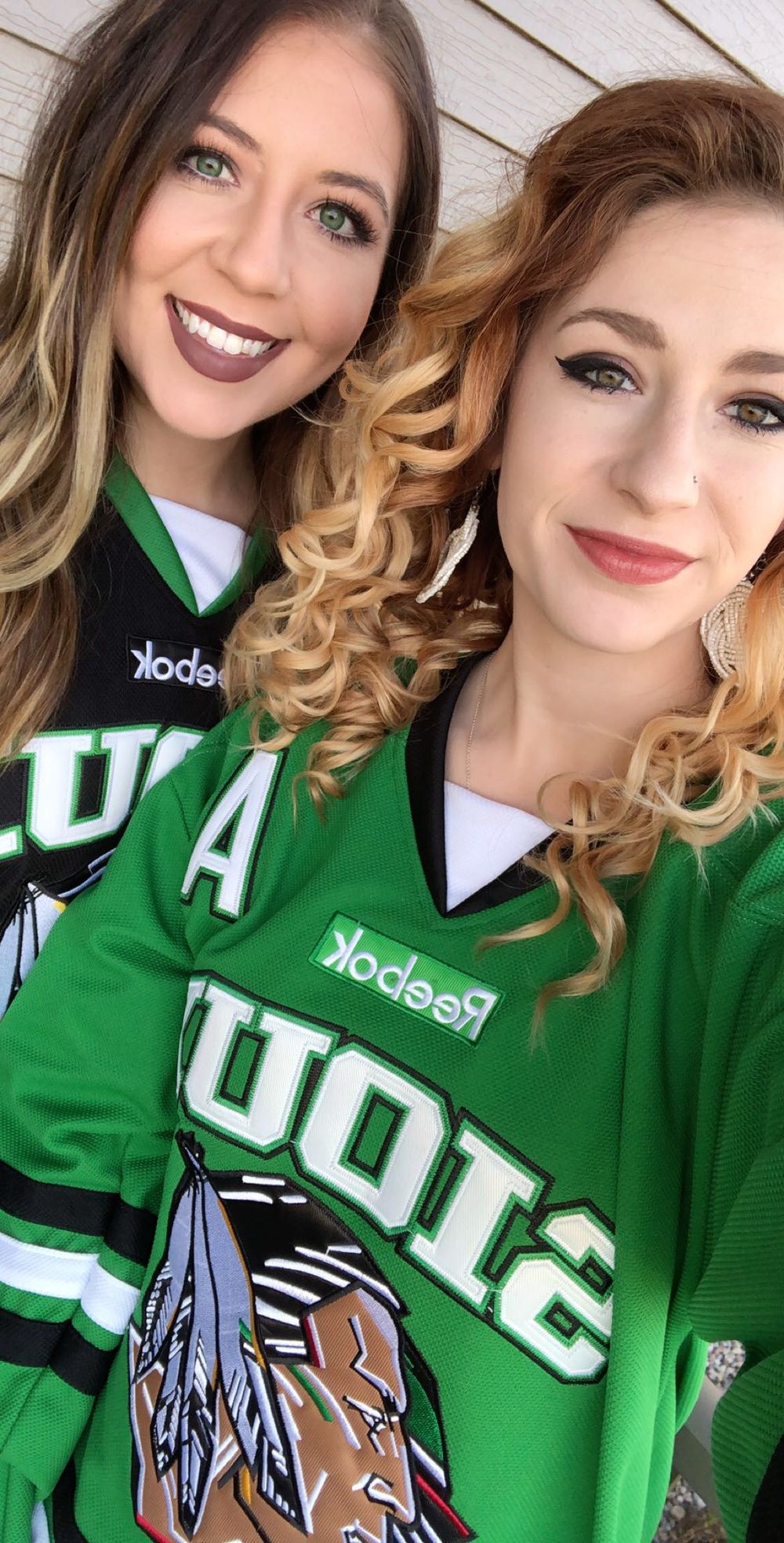 Two smiling women wearing green Reebok hockey jerseys take a selfie together.