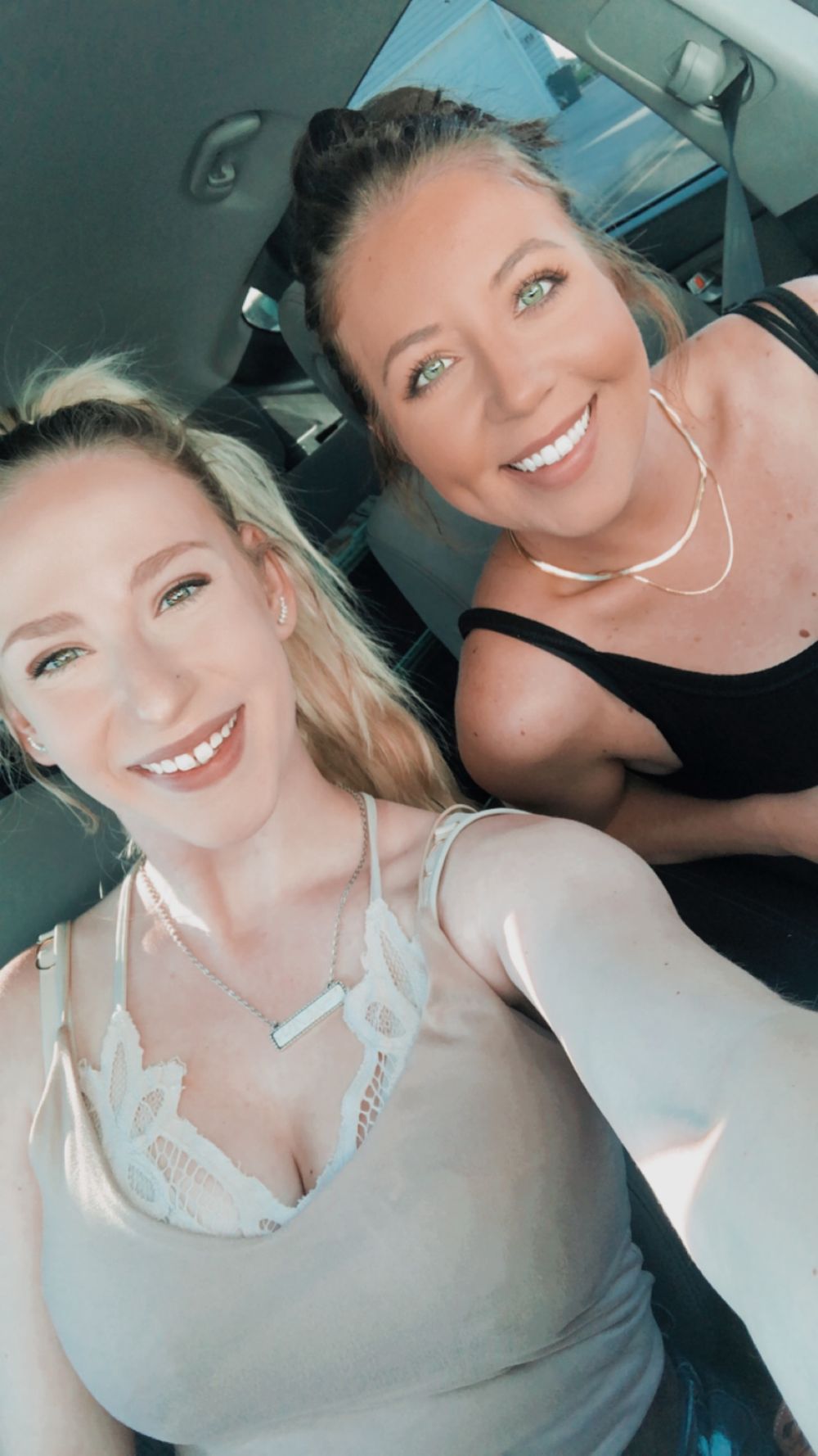Two smiling blonde women taking a selfie together inside a car on a sunny day.
