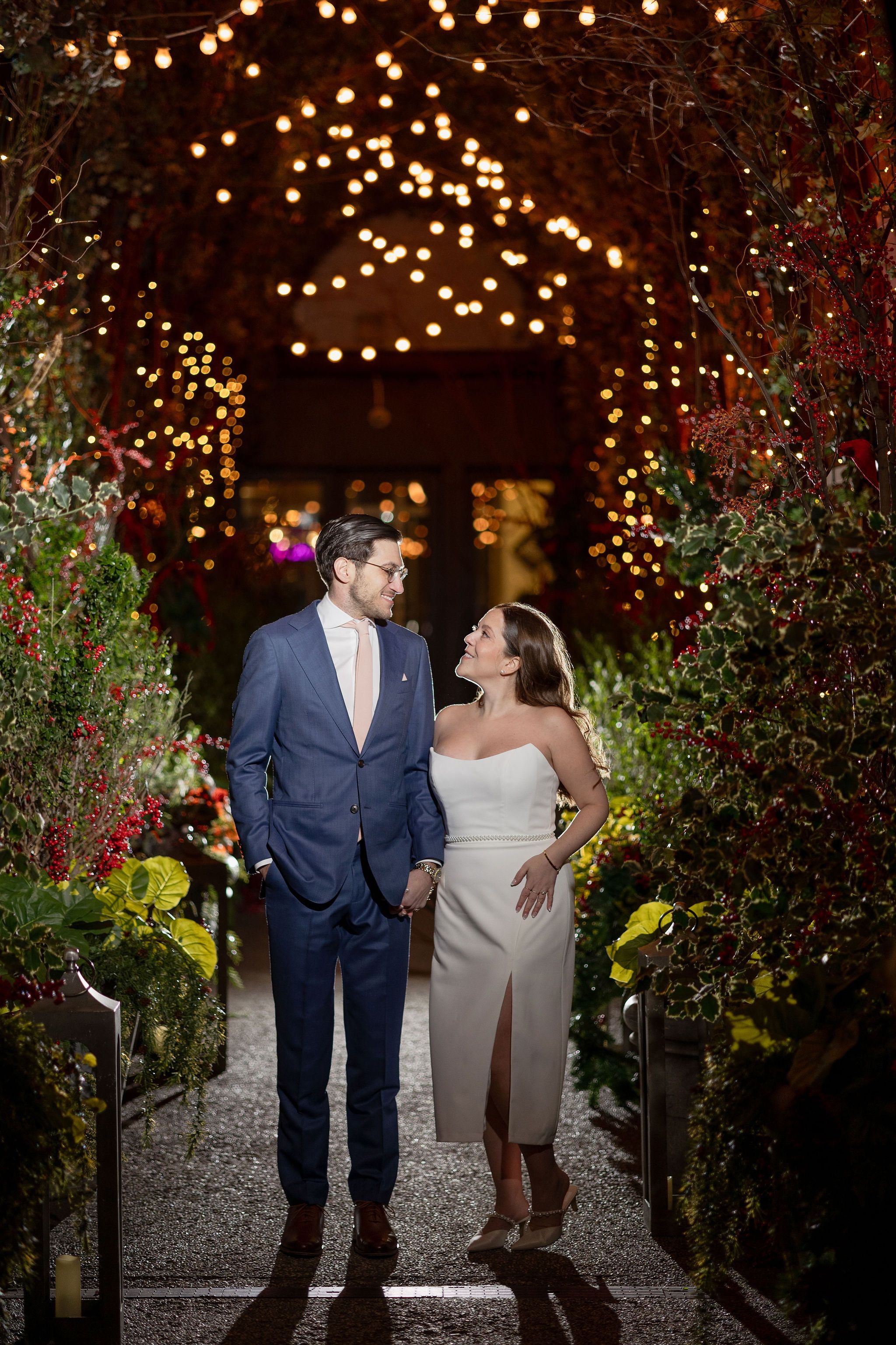 Couple sharing romantic moment under twinkling lights in garden pathway.