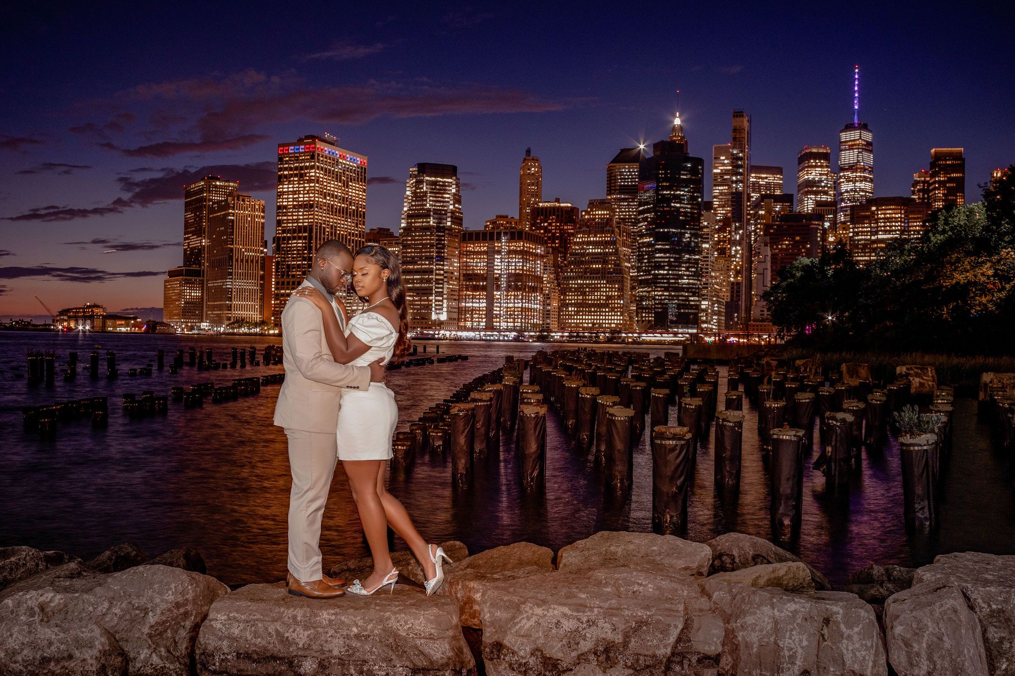 A romantic moment at sunset overlooking the illuminated New York City skyline from Brooklyn Bridge Park.