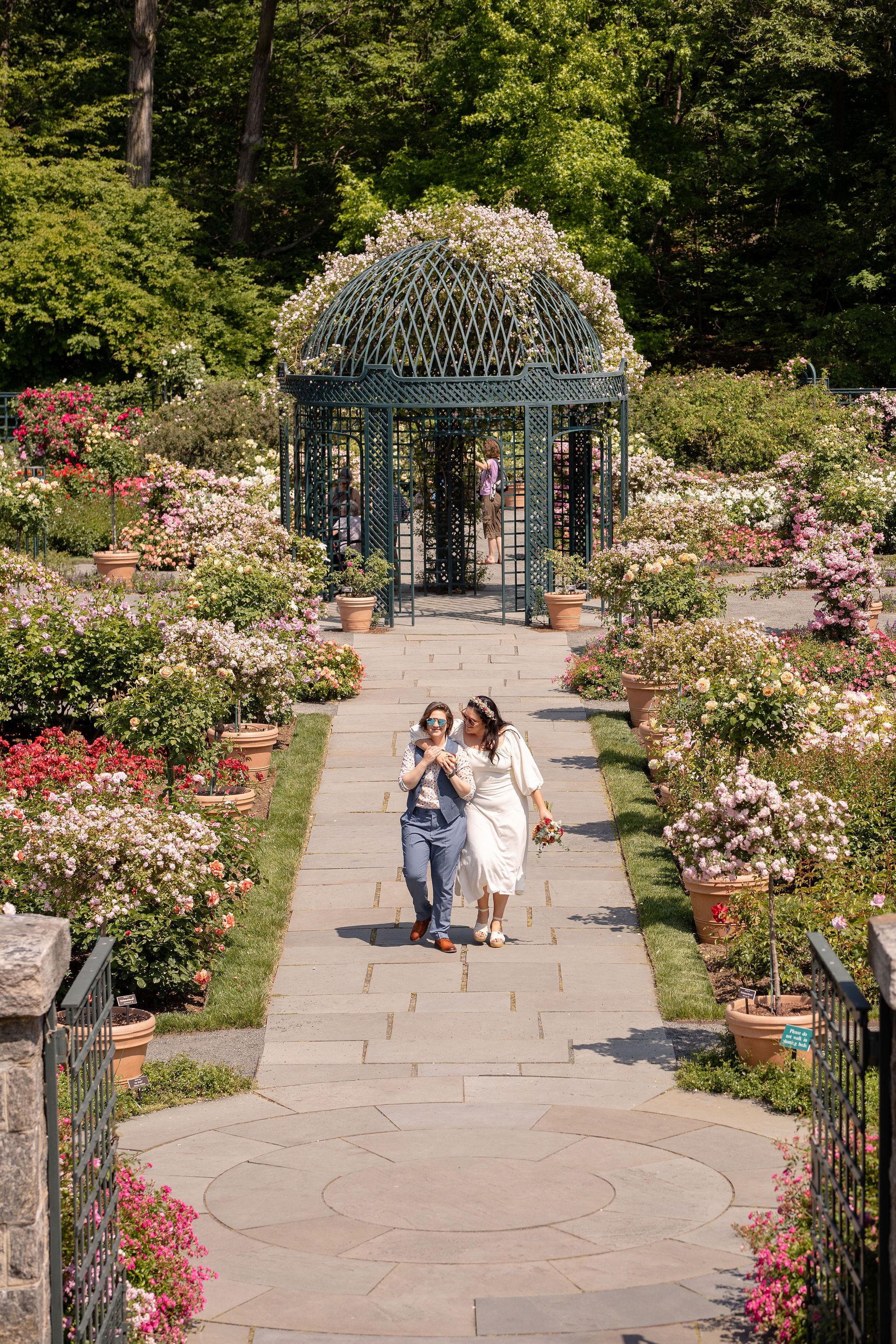 A garden path leading to an ornate metal gazebo surrounded by blooming flowers.