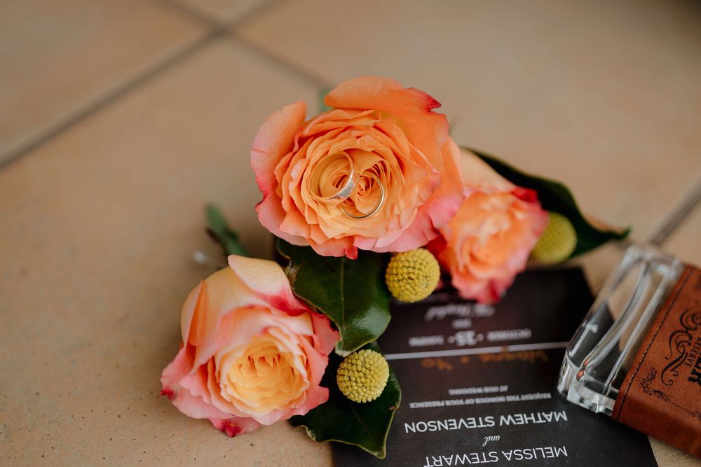 Wedding rings rest on peach roses beside an invitation for Melissa Stevenson and Mathew Stewart.
