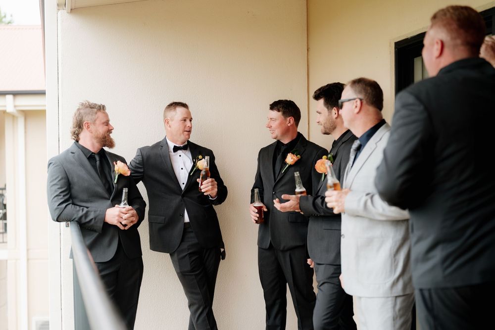 Groom and groomsmen in suits with floral boutonnieres laughing and celebrating together before the wedding.