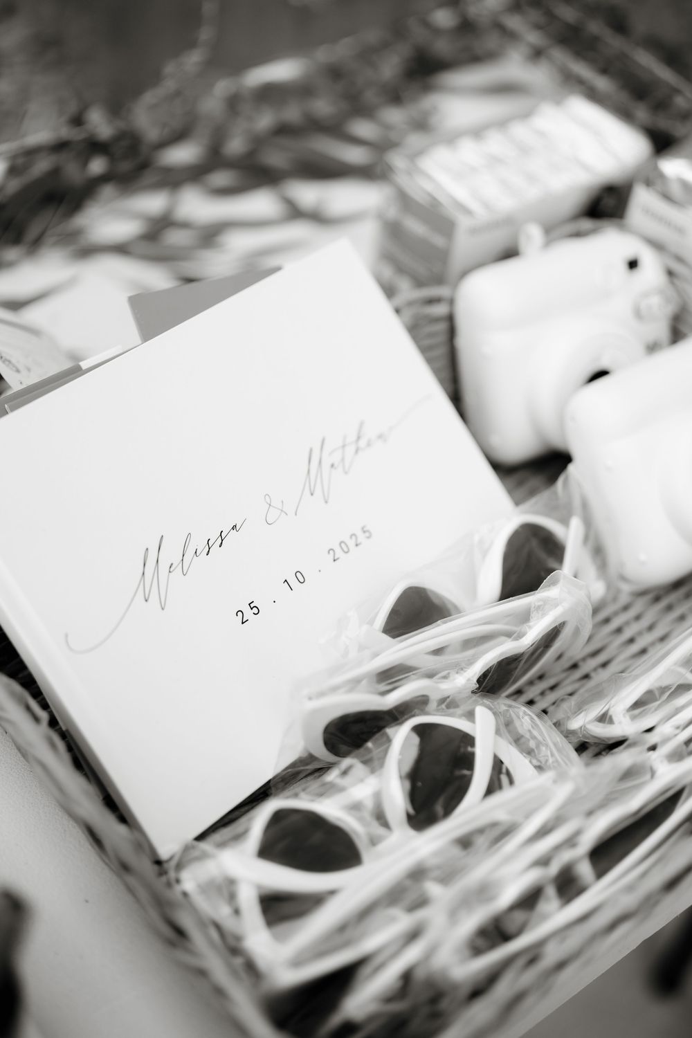 Black and white wedding favor box with card reading Melissa & Matteo 25.10.2025, featuring sunglasses and white AirPods.