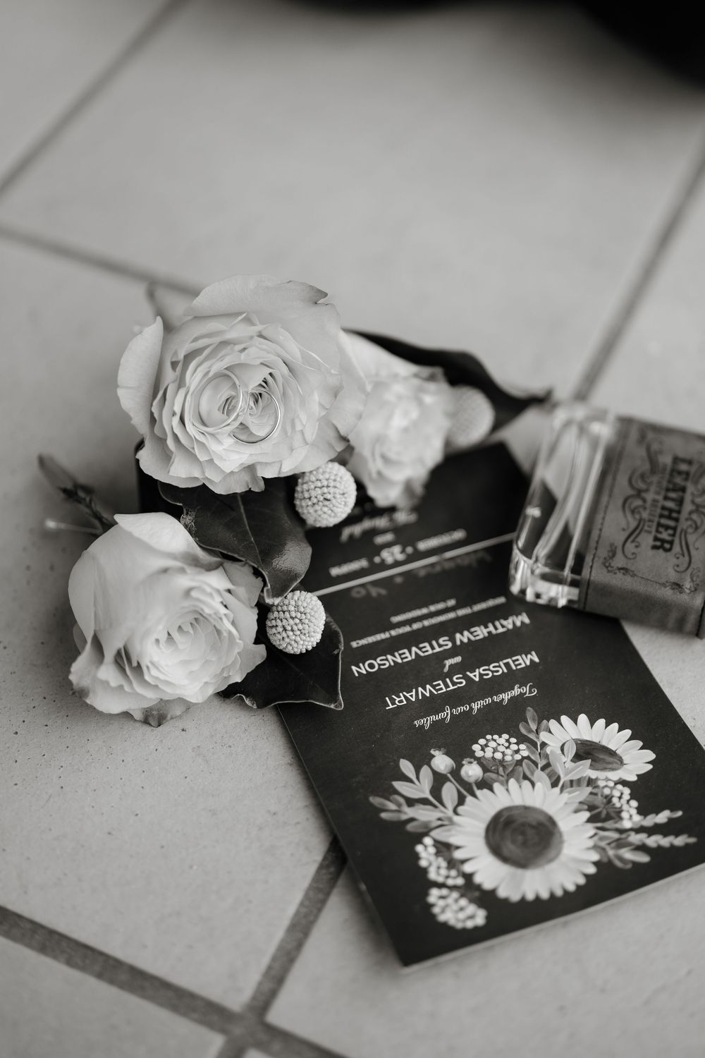 Black and white wedding flat lay with roses, rings, sunflower invitation for Mathew Stevenson and Melissa Stewart.