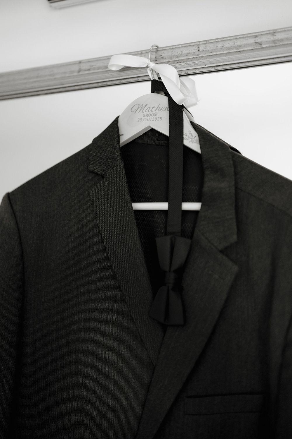 Black suit jacket with bow tie hanging on a branded hanger in a closet, perfect for formal occasions.