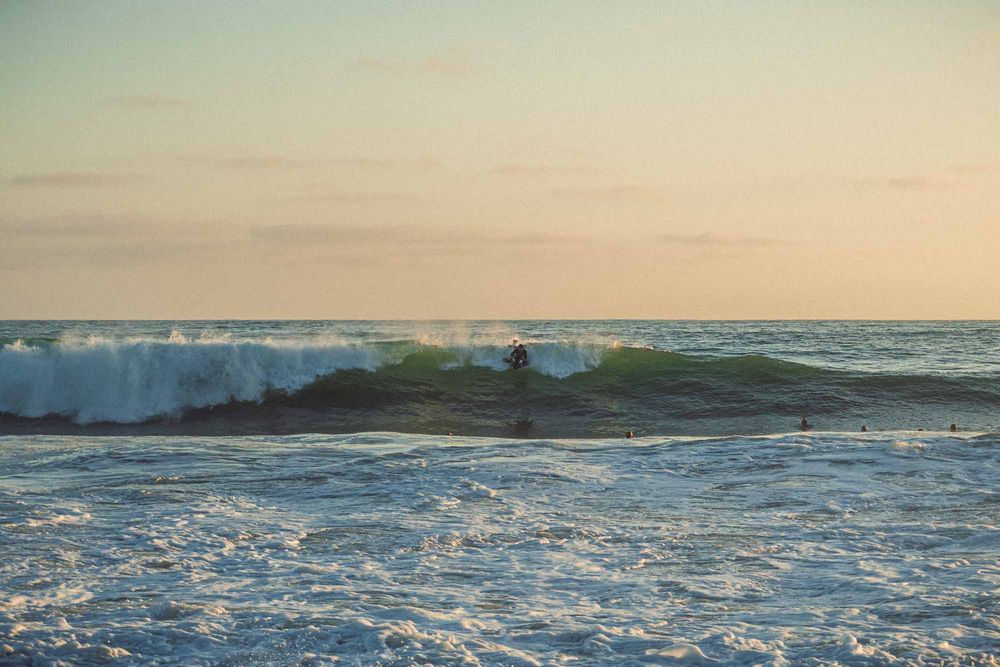 Lone surfer riding a green wave in the ocean during a peaceful pastel sunset.
