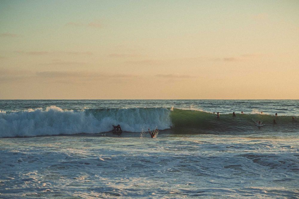Surfers navigating large rolling ocean waves during a warm golden hour sunset.