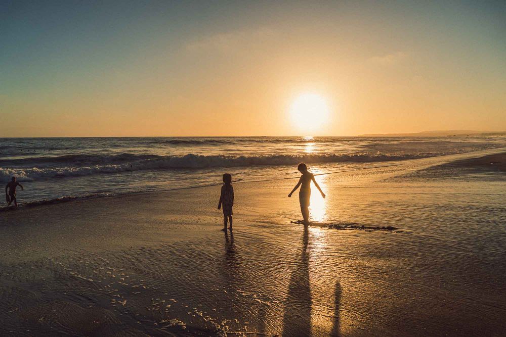 Two children silhouetted playing on a reflective beach during a stunning golden sunset.