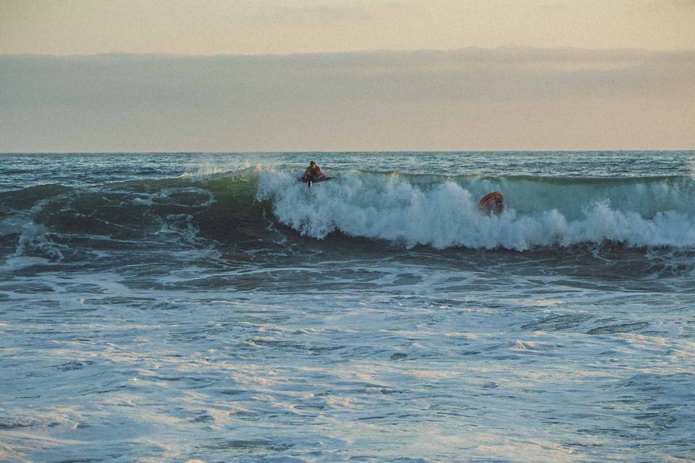 Bodyboarder riding powerful ocean waves during dusk at a scenic coastal beach.