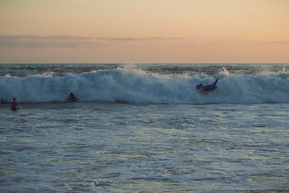Surfers navigate large breaking waves in the ocean during a golden sunset.