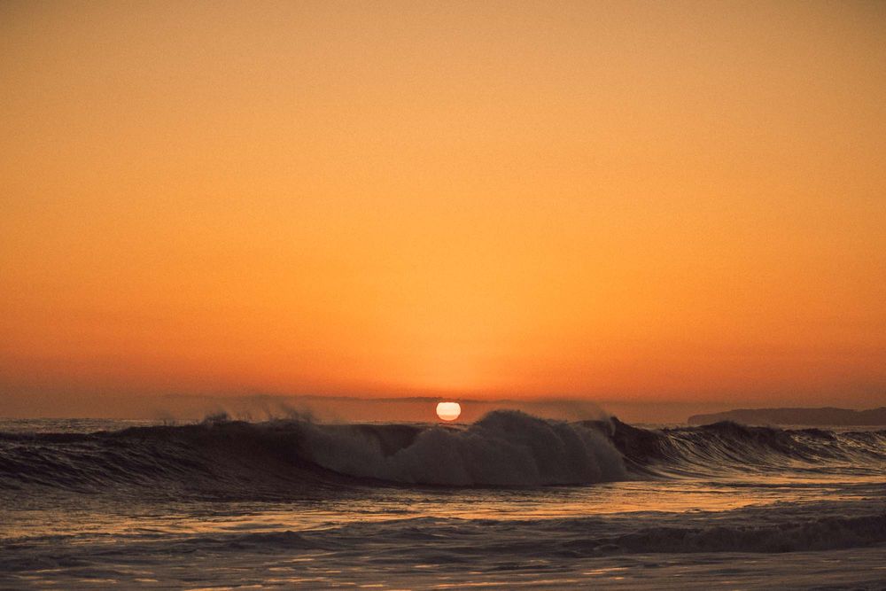 Golden sunset over ocean waves with vibrant orange sky and sun setting on the horizon.