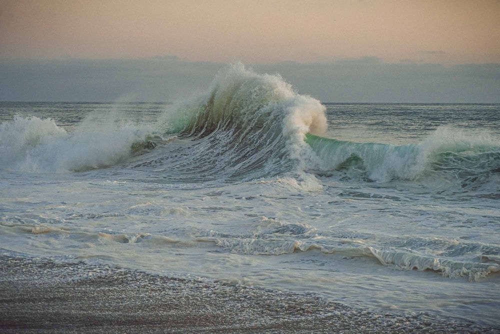 Large powerful ocean wave crashing on a sandy beach at sunset with seafoam and misty spray.