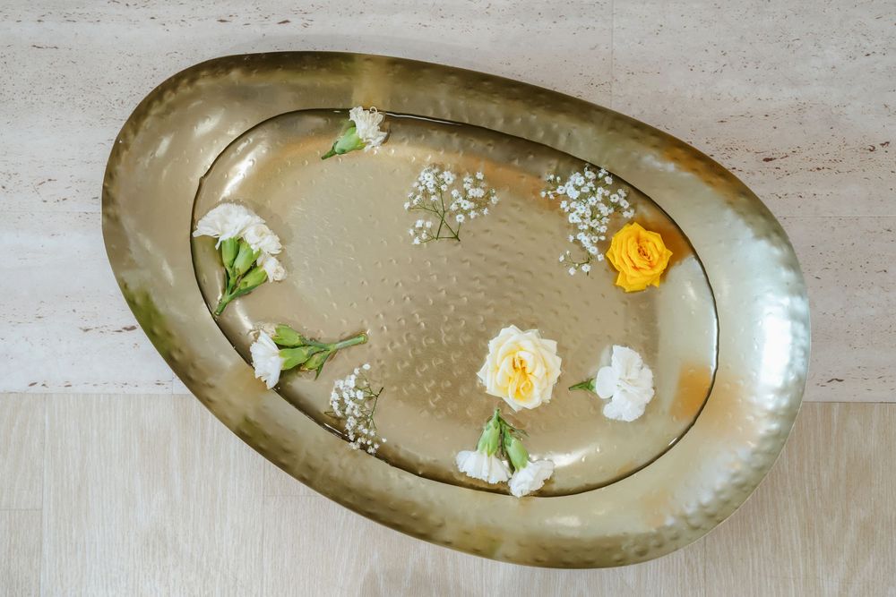 Gold oval hammered metal tray with white and yellow flowers arranged elegantly on a wooden surface.