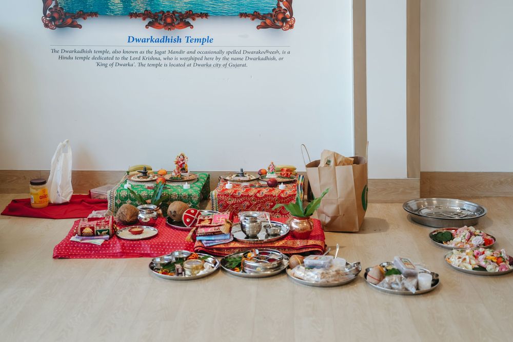 Traditional Hindu puja offerings arranged on red cloth at Dwarkadish Temple, featuring plates of food, flowers, and ritual items.