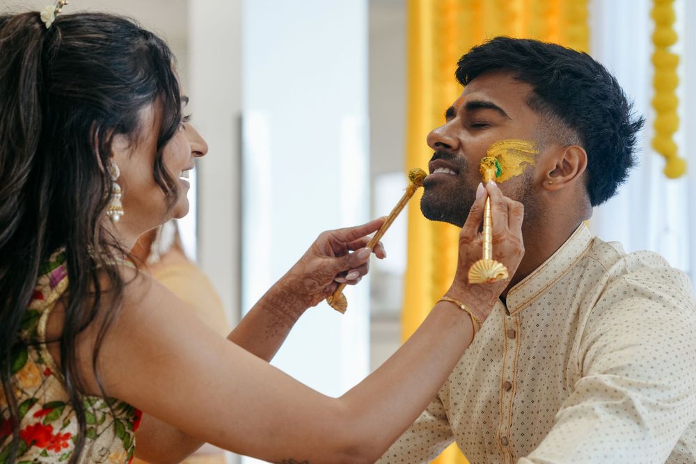 A woman applies turmeric paste to a smiling man's face during a traditional Indian Haldi wedding ceremony.