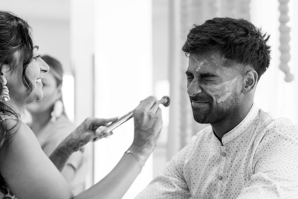 Black and white photo of a groom having makeup applied by a makeup artist before his wedding ceremony.