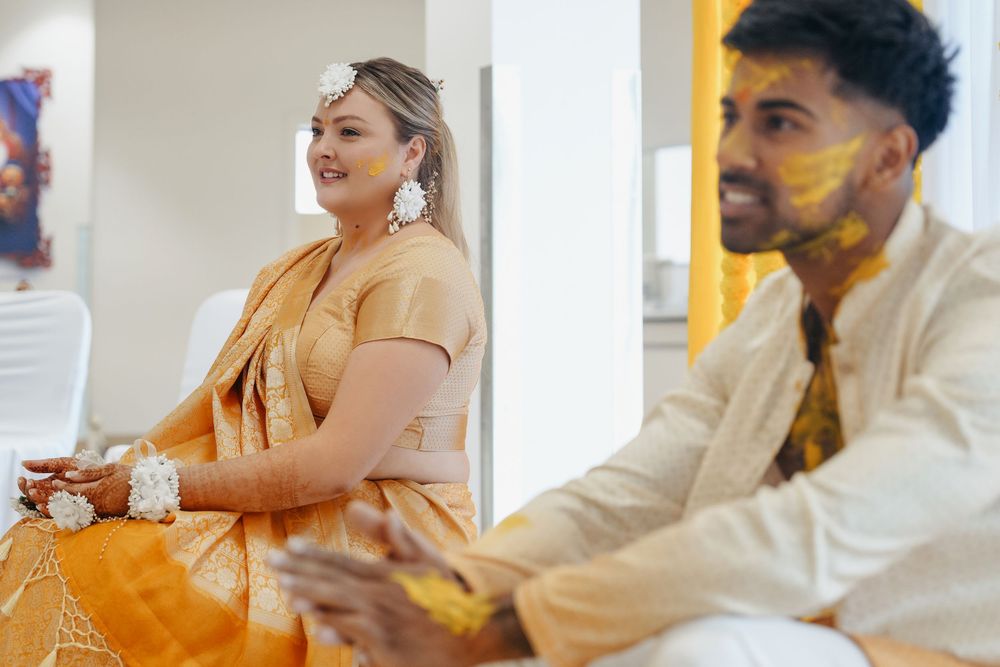 Couple in traditional Indian attire with haldi ceremony turmeric on their faces and hands during wedding celebration.