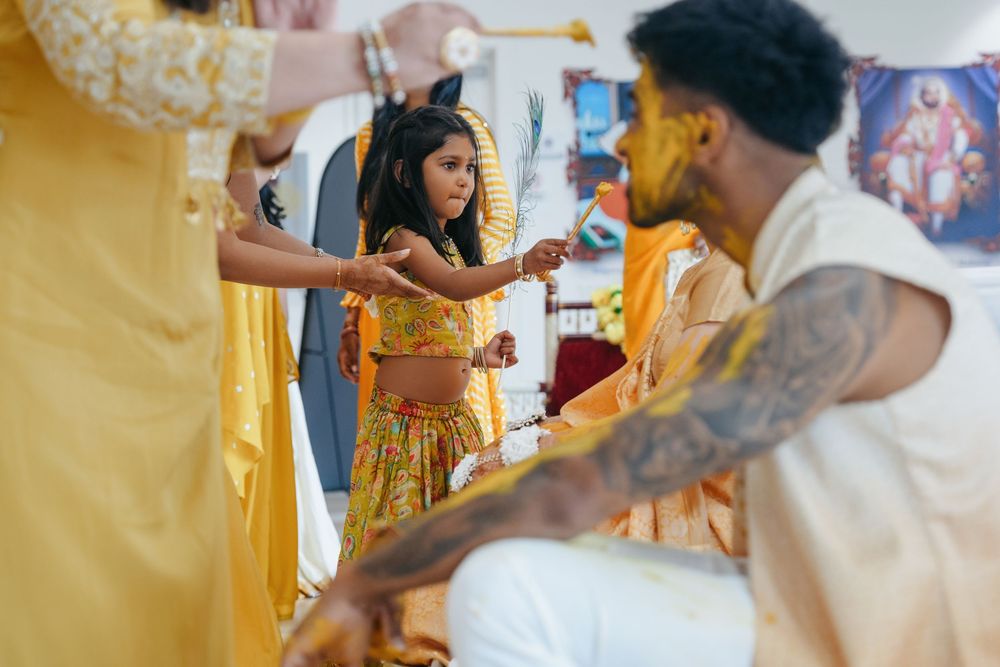 A woman in a yellow lehenga participates in a traditional Indian Haldi ceremony with guests in vibrant attire.