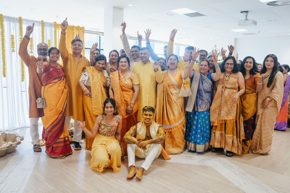 Large Indian family group photo in vibrant yellow and orange traditional attire celebrating a wedding ceremony together.